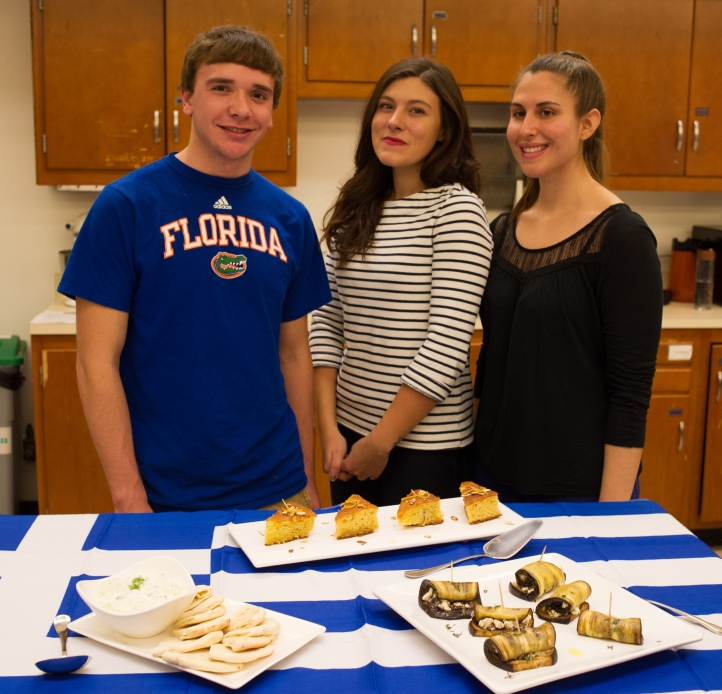 Three students stand behind a table displaying dishes they prepared in a kitchen classroom