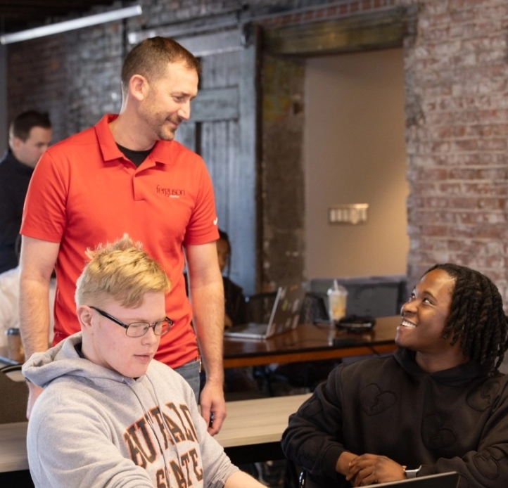 Smiling teacher chats with students at a shared desk in a modern classroom