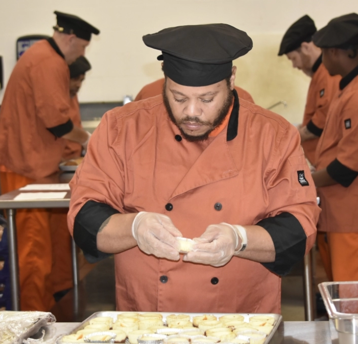 Students in culinary uniforms practice food preparation in a commercial training kitchen