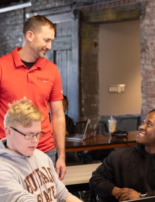 Smiling teacher chats with students at a shared desk in a modern classroom